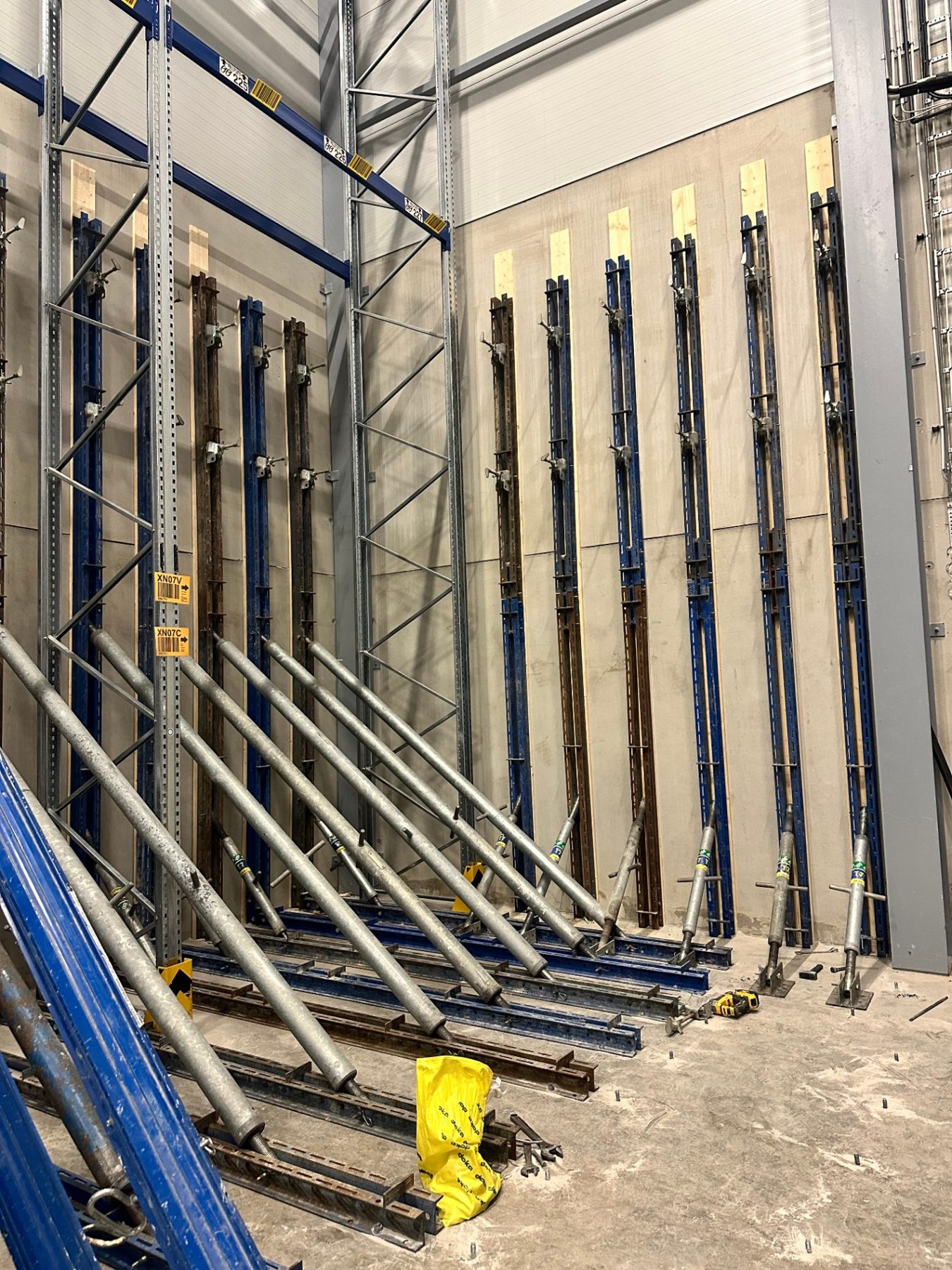 Braced steel uprights and props supporting concrete wall panels inside a warehouse