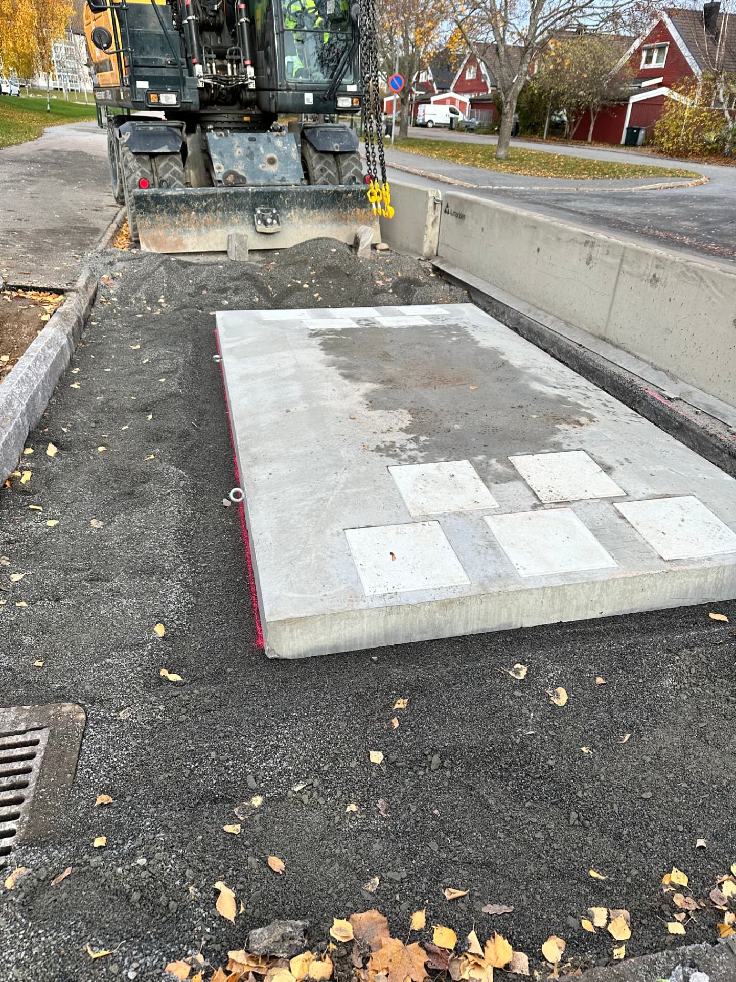 Excavator lowering a precast concrete platform slab into a prepared bed