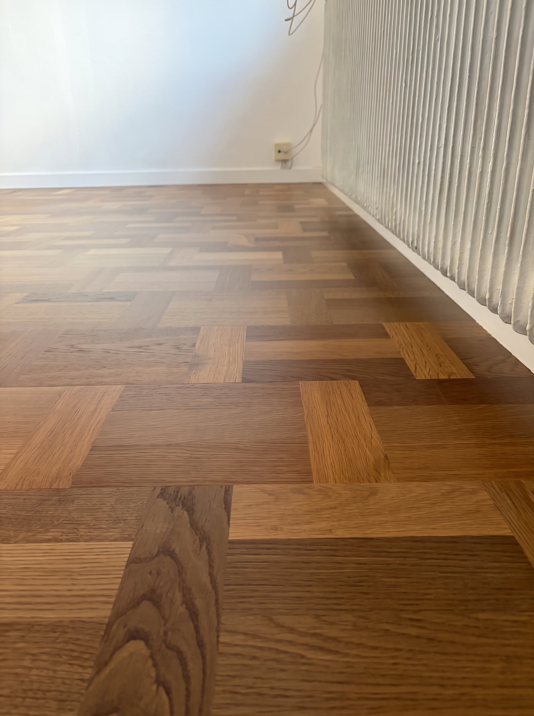 Close view of finished oak parquet meeting a painted skirting and radiator