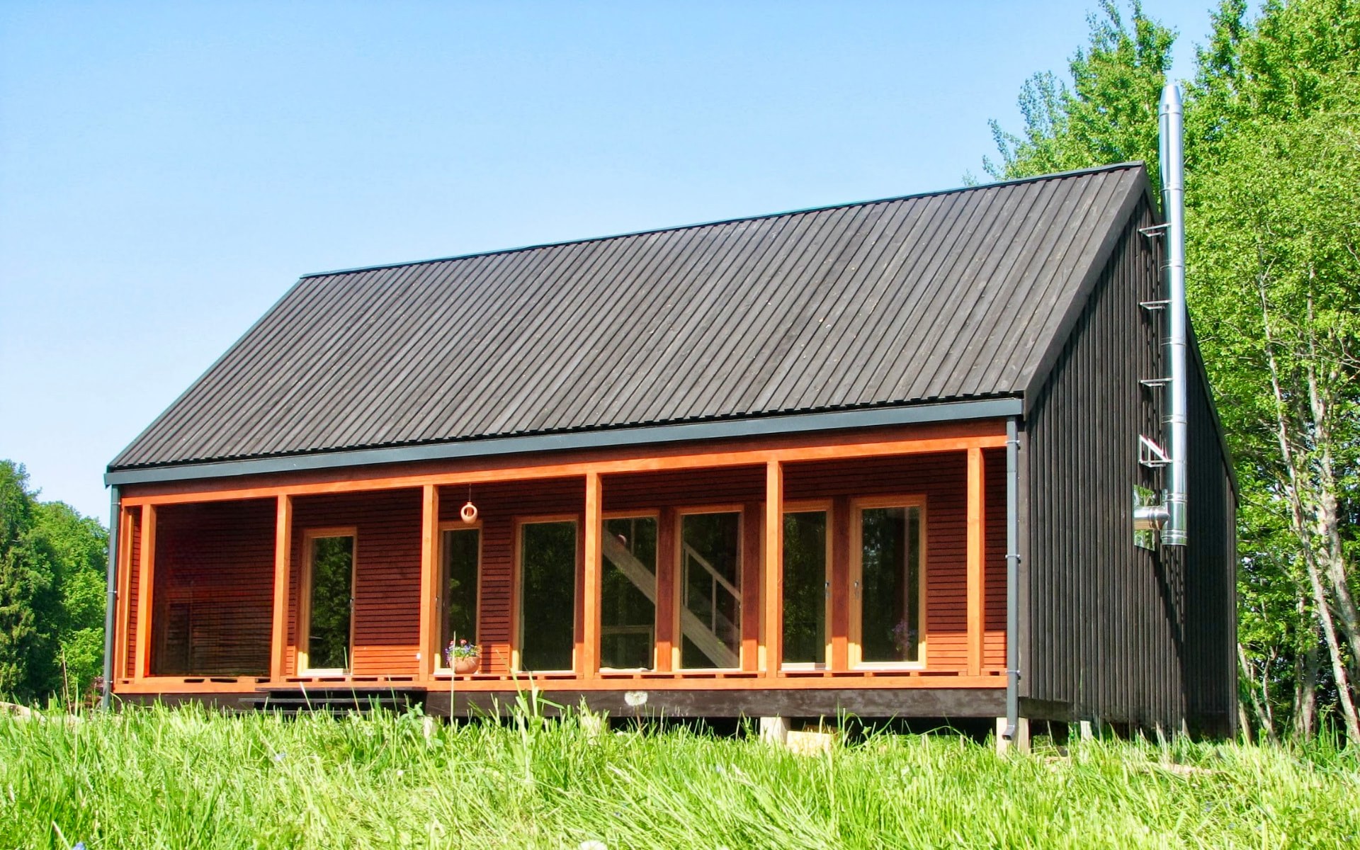 Black timber summer house with a warm cedar glazed veranda in a meadow