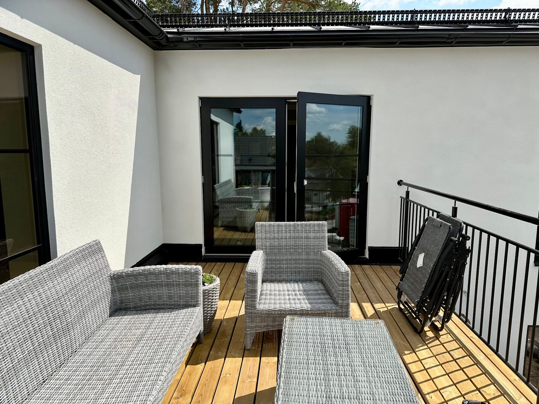 Timber roof terrace with lounge furniture between white rendered walls and black-framed doors