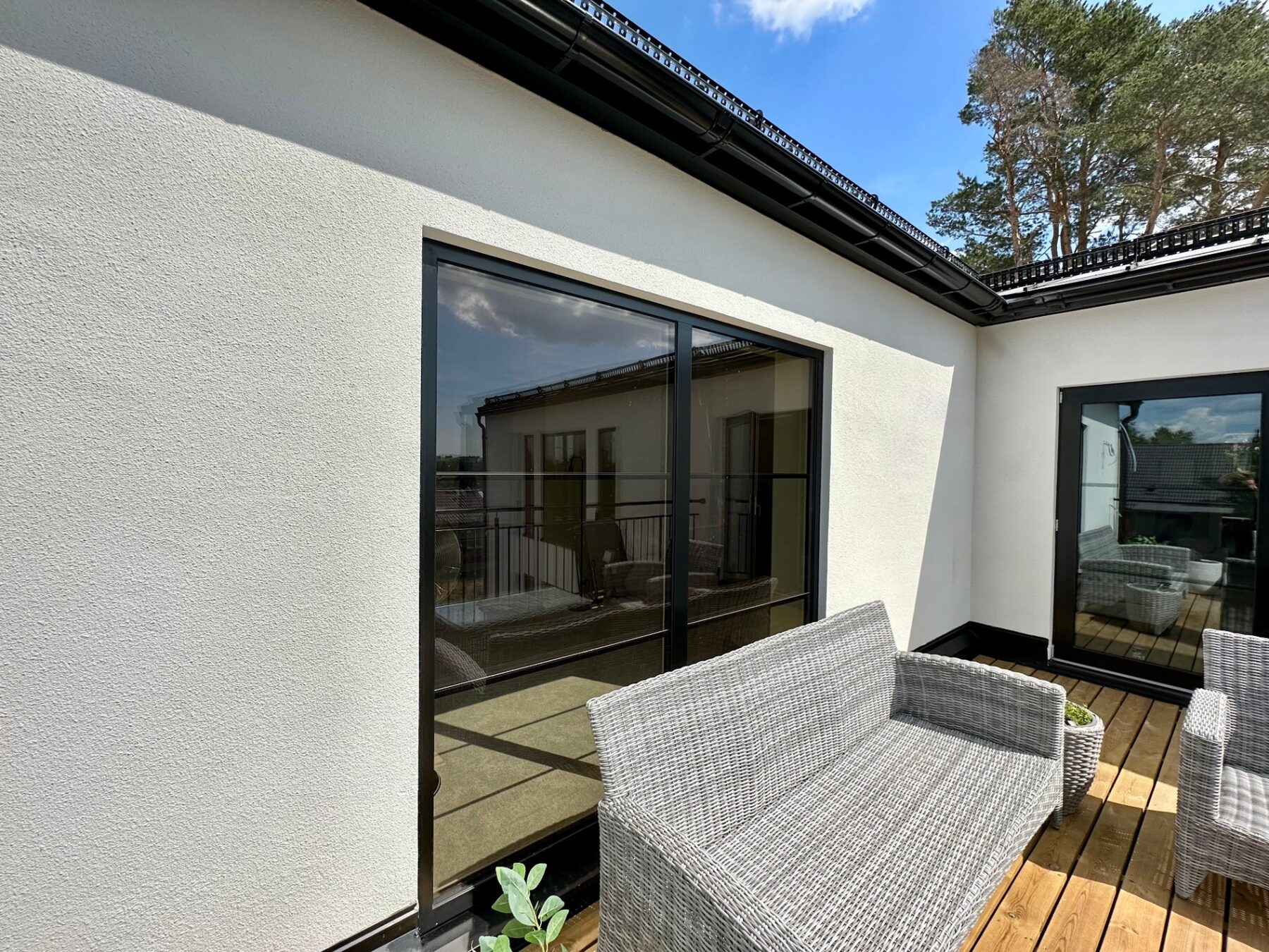 Roof terrace decking meeting full-height black sliding doors on a white rendered wall