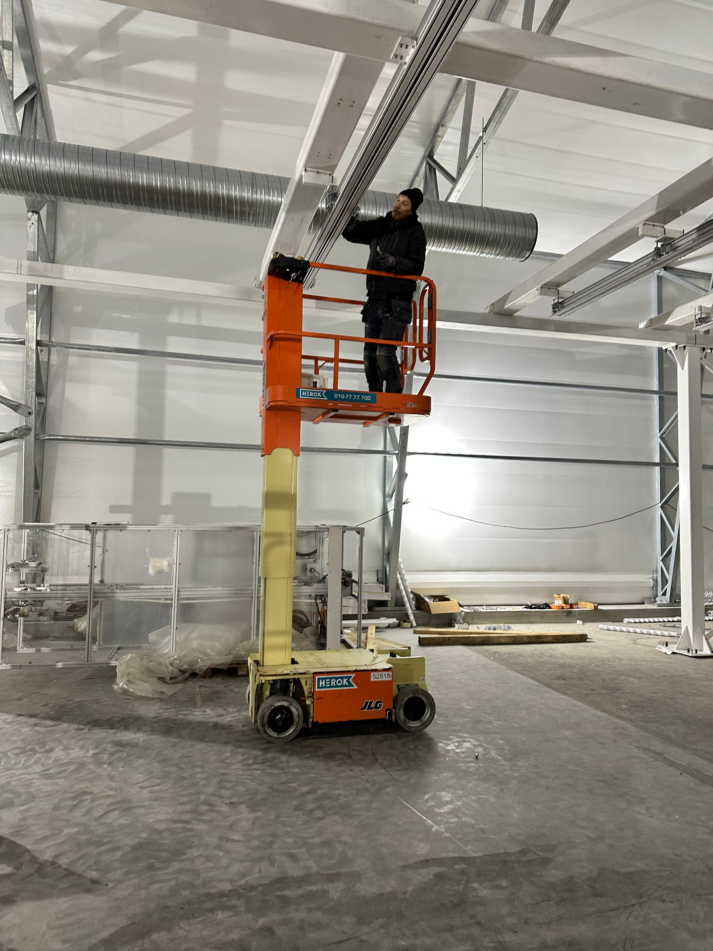 Worker on a mast lift fixing spiral ventilation ductwork to the roof structure